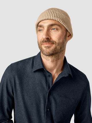 A man wearing a Beanie Khaki and a dark blue collared shirt looks off to the side.