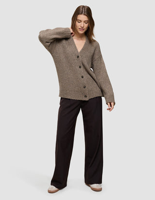A woman wearing a Women’s Chunky Soft Wool Knit Cardigan Taupe Melange, a cozy V-neck button-down, and dark trousers.