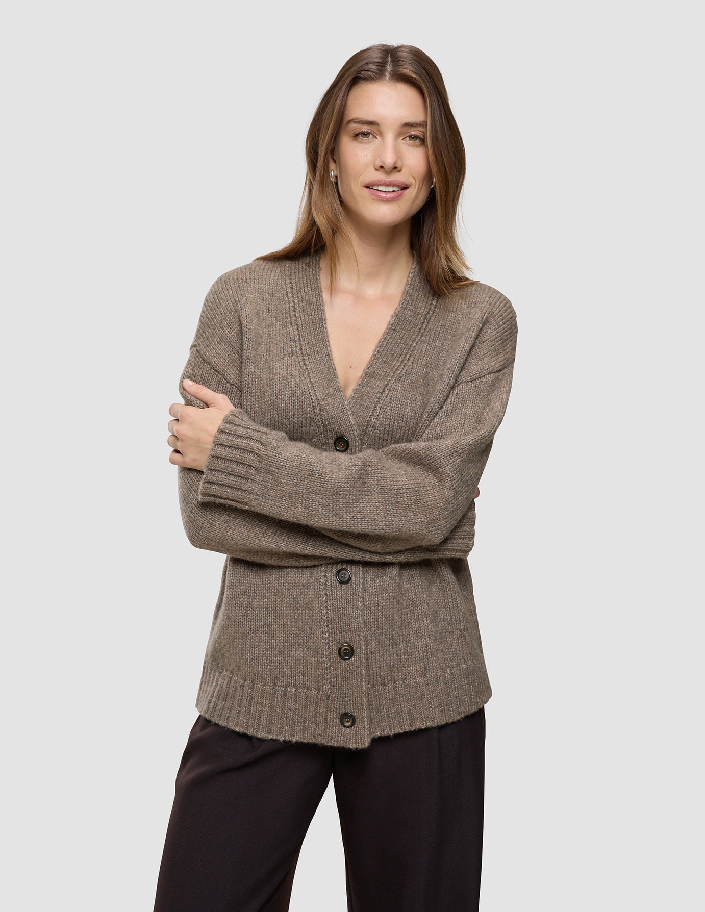 A woman wearing a cozy Women’s Chunky Soft Wool Knit Cardigan Taupe Melange, featuring a V-neck, button-down front, and ribbed cuffs and hem.