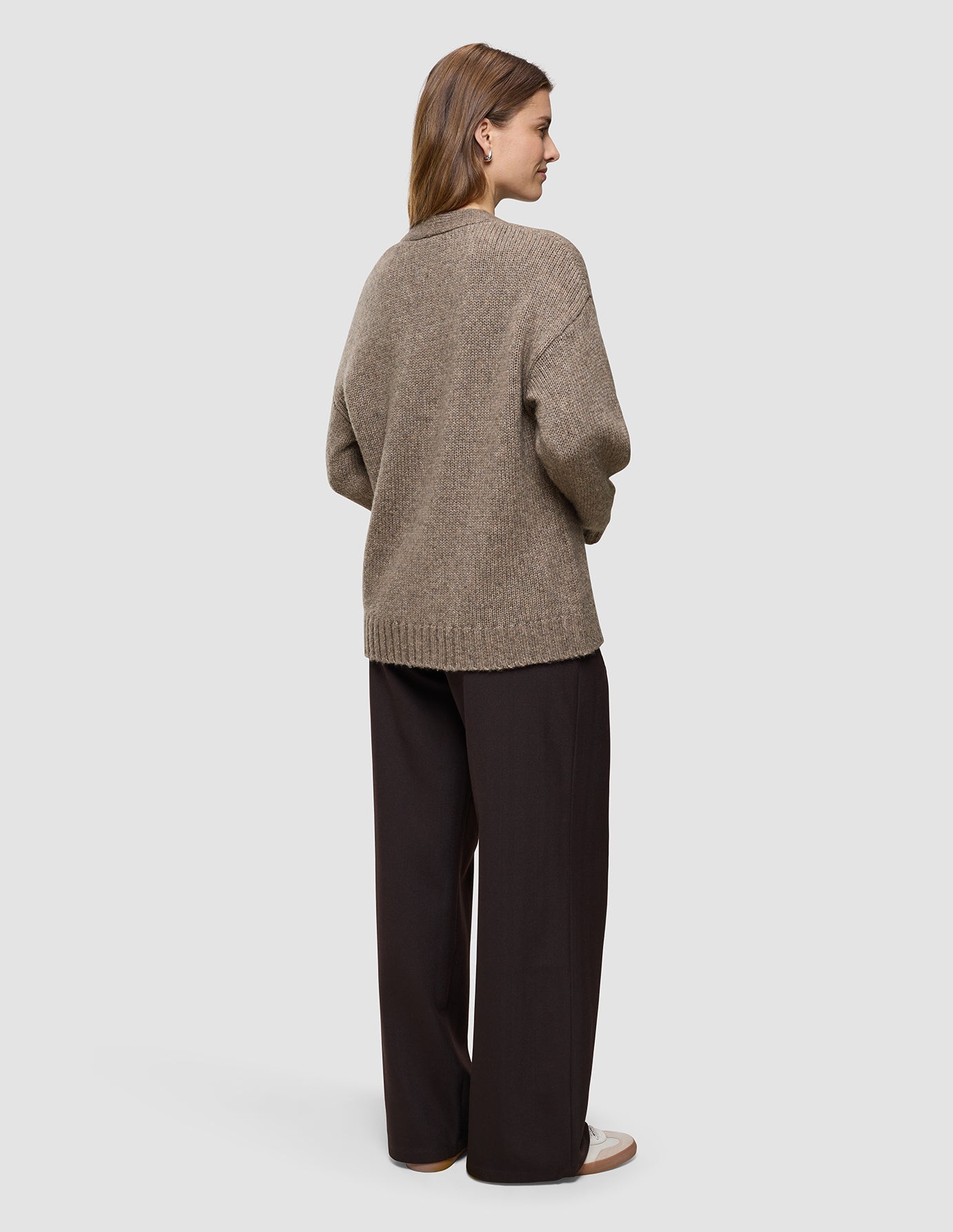 Woman seen from behind wearing a cozy Women’s Chunky Soft Wool Knit Cardigan Taupe Melange and dark brown trousers.