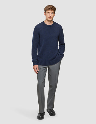 A man wears a Chunky Soft Wool Knit Crewneck Dark Navy Melange sweater with grey trousers and black shoes.