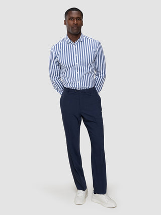 A man wearing a Classic Shirt Dusky Blue Stripe Regular, navy trousers, and white sneakers.
