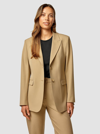 A woman wearing an Essential Blazer Caramel over a black top.
