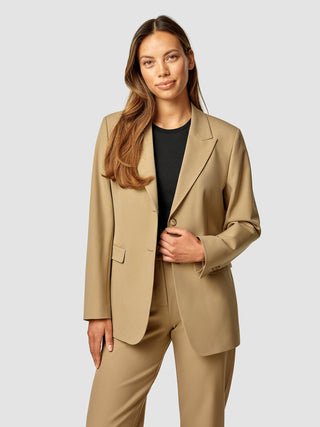 A woman wearing an Essential Blazer Caramel over a black top.