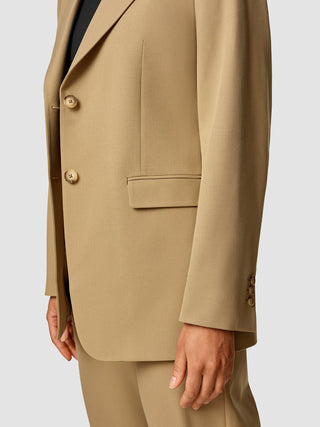 A person wearing an Essential Blazer Caramel over a black top.