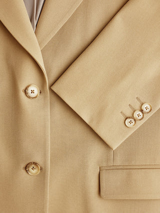 Close-up of the Essential Blazer Caramel in tan, showing the lapel, sleeve cuff with button detail, and a pocket.
