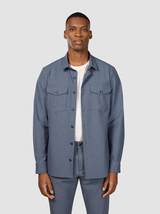 A man wearing an Essential Overshirt Storm Blue Melange featuring two chest pockets over a white t-shirt.
