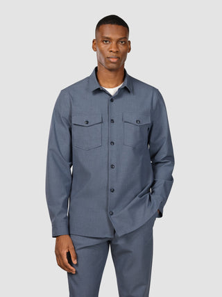 A man wearing an Essential Overshirt Storm Blue Melange with two chest pockets and matching trousers, reflecting a clean Scandinavian design.