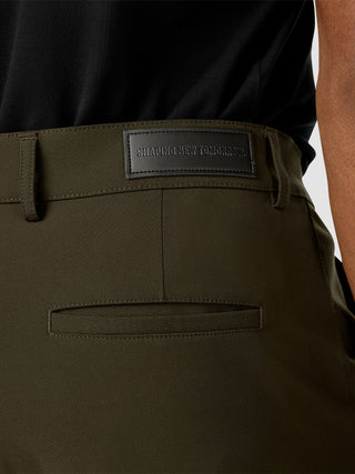 A close-up of dark olive Essential Pants Slim Bavarian Green featuring a black label on the waistband that reads SHAPING NEW TOMORROW.