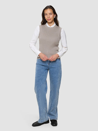 A woman wearing a Women’s Fine Knit Rib Vest Dark Sand over a white button-down shirt, blue jeans, and black loafers.