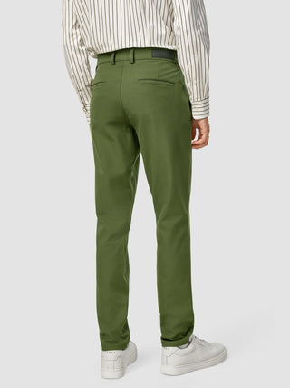 A person seen from behind wearing olive green GEN2™ Pants Slim Rainforest with a twill texture, a striped button-down shirt, and white sneakers.