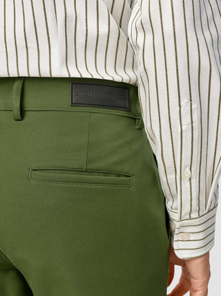 A person wearing olive green GEN2™ Pants Slim Rainforest with a Shaping New Tomorrow brand tag on the waistband and a white shirt with vertical green stripes, featuring a subtle twill texture.