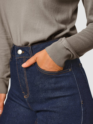 A person wearing a grey long-sleeved shirt tucked into Jeans Straight Fit Dark Blue with their hand in the pocket.