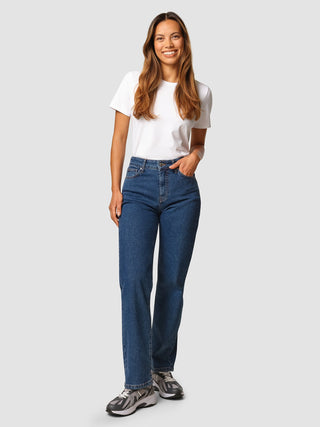A smiling woman wears a white t-shirt and Jeans Straight Fit Medium Blue with sneakers.