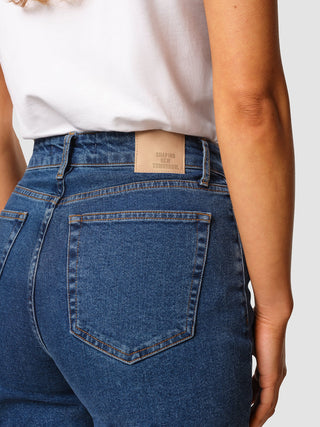 A person wearing Jeans Straight Fit Medium Blue with a leather patch on the waistband that reads SHAPING NEW TOMORROW.