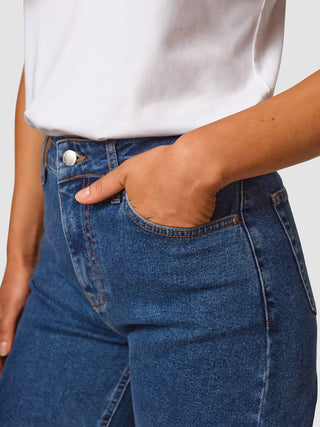 A person wearing a white t-shirt tucked into Jeans Straight Fit Medium Blue, with one hand resting in the pocket.