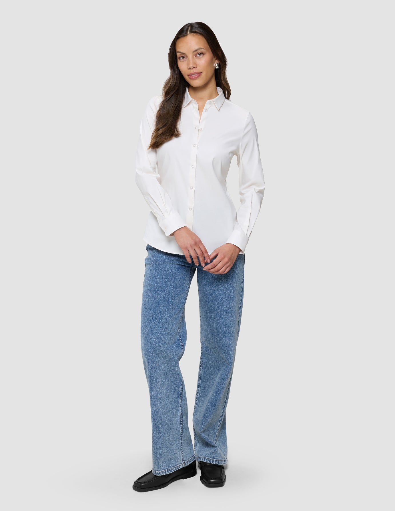 A woman wearing a Women’s Oxford Shirt White Orchid Slim tucked into light-wash blue jeans and black loafers.
