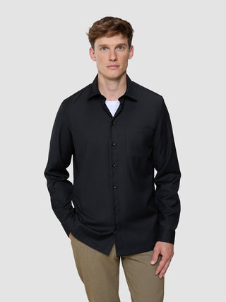 A man wearing a Siena Shirt Black button-down over a white undershirt with tan trousers.