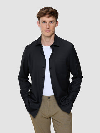 A man wearing a lightweight Siena Shirt Black unbuttoned over a white t-shirt and tan trousers.