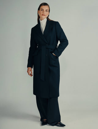 A person wearing a Women’s Wool Coat Black in a Scandinavian design over a white turtleneck sweater and black trousers.