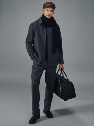 A man in a Heritage Overshirt Stone Grey and black scarf holding a black duffel bag.