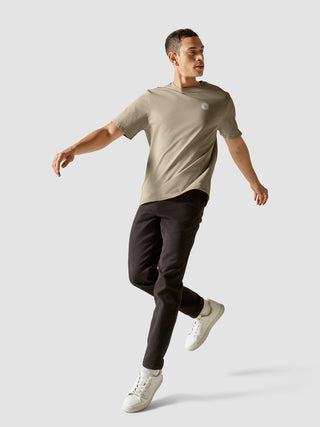 A man wearing a Supima T-shirt Box Fit Globe Sahara and dark pants jumping in mid-air.