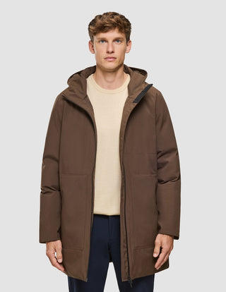 A person wearing a hooded, saddle brown Utility Jacket over a cream-colored sweater and dark trousers.