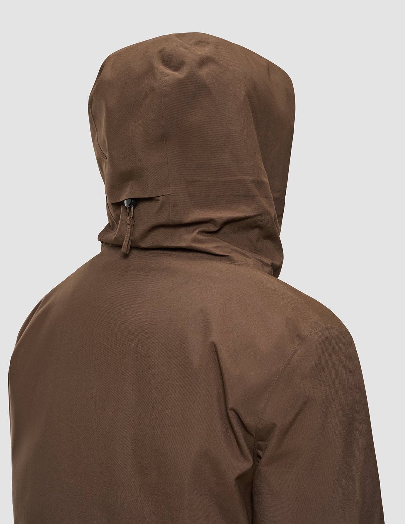 Back view of a person wearing a brown Utility Jacket Saddle Brown, a recycled polyester hooded jacket with a toggle adjustment at the nape of the neck.