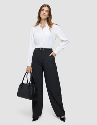 A woman wearing a white Golden Contrast blouse and black Avira Wide Pants holds a black handbag.