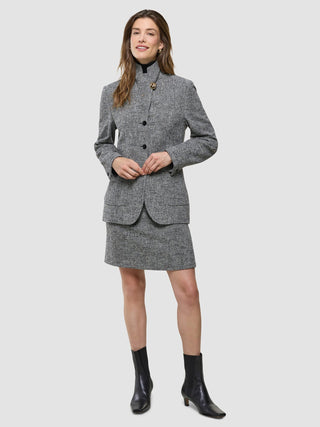 A woman models a gray Women Ashryn Short Skirt Domino Herringbone and matching blazer with a black turtleneck and black heeled boots.