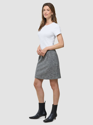 A woman wearing a white t-shirt, a Women Ashryn Short Skirt Domino Herringbone, and black ankle boots stands against a plain background.