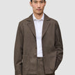 A man wearing a dark beige Atelier Overshirt heavyweight twill blazer over a white collared shirt.