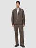A person wearing an Atelier Overshirt Dark Beige with matching trousers over a white collared shirt, styled with dark loafers for a clean Scandinavian design aesthetic.