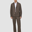 A person wearing an Atelier Overshirt Dark Beige with matching trousers over a white collared shirt, styled with dark loafers for a clean Scandinavian design aesthetic.