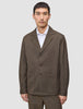 A man wears a brown Atelier Overshirt Dark Beige heavyweight twill blazer with large patch pockets over a white collared shirt.