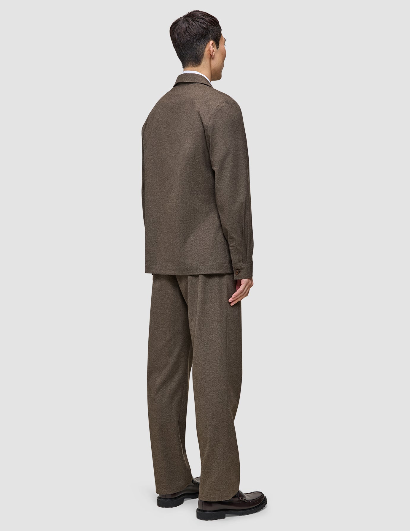 A man viewed from behind, wearing an Atelier Overshirt Dark Beige and matching trousers in a Scandinavian design.