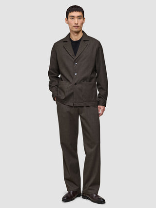 A person wearing a dark brown, heavyweight textured Atelier Overshirt with a notched collar and matching trousers, paired with a black crew-neck shirt and dark shoes.