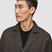 A man wears an Atelier Overshirt Dark Brown made of heavyweight textured fabric over a black crew neck shirt in a Scandinavian design.