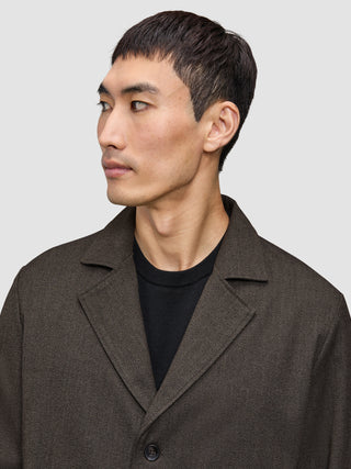 A man wears an Atelier Overshirt Dark Brown made of heavyweight textured fabric over a black crew neck shirt in a Scandinavian design.