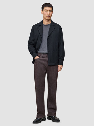 A man wearing a dark navy Atelier Overshirt over a grey t-shirt, dark trousers, and black dress shoes.