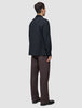 A person seen from behind, wearing an Atelier Overshirt Dark Navy in a heavyweight texture, paired with dark brown trousers and black dress shoes.
