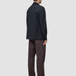 A person seen from behind, wearing an Atelier Overshirt Dark Navy in a heavyweight texture, paired with dark brown trousers and black dress shoes.
