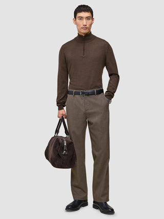 A man wears a brown quarter-zip sweater and Atelier Pants Relaxed Dark Beige in heavyweight broken twill, paired with a black belt, boots, and a brown duffel bag.