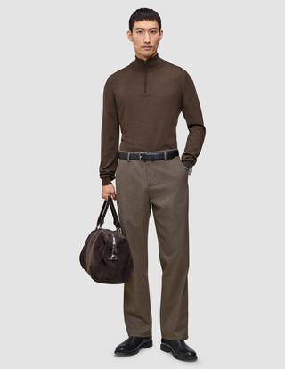 A man wears a brown quarter-zip sweater and Atelier Pants Relaxed Dark Beige in heavyweight broken twill, paired with a black belt, boots, and a brown duffel bag.