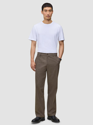 A man wearing a white t-shirt, black shoes, and Atelier Pants Relaxed Dark Beige in heavyweight broken twill.