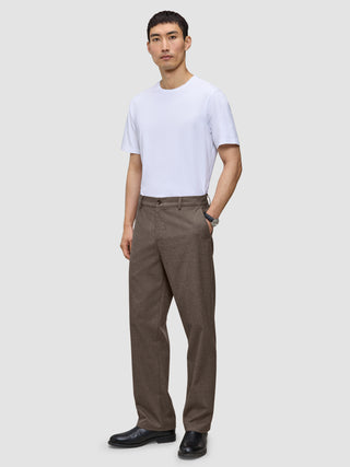 A man wearing a white t-shirt and Atelier Pants Relaxed Dark Beige in a heavyweight broken twill, finished with black leather shoes.