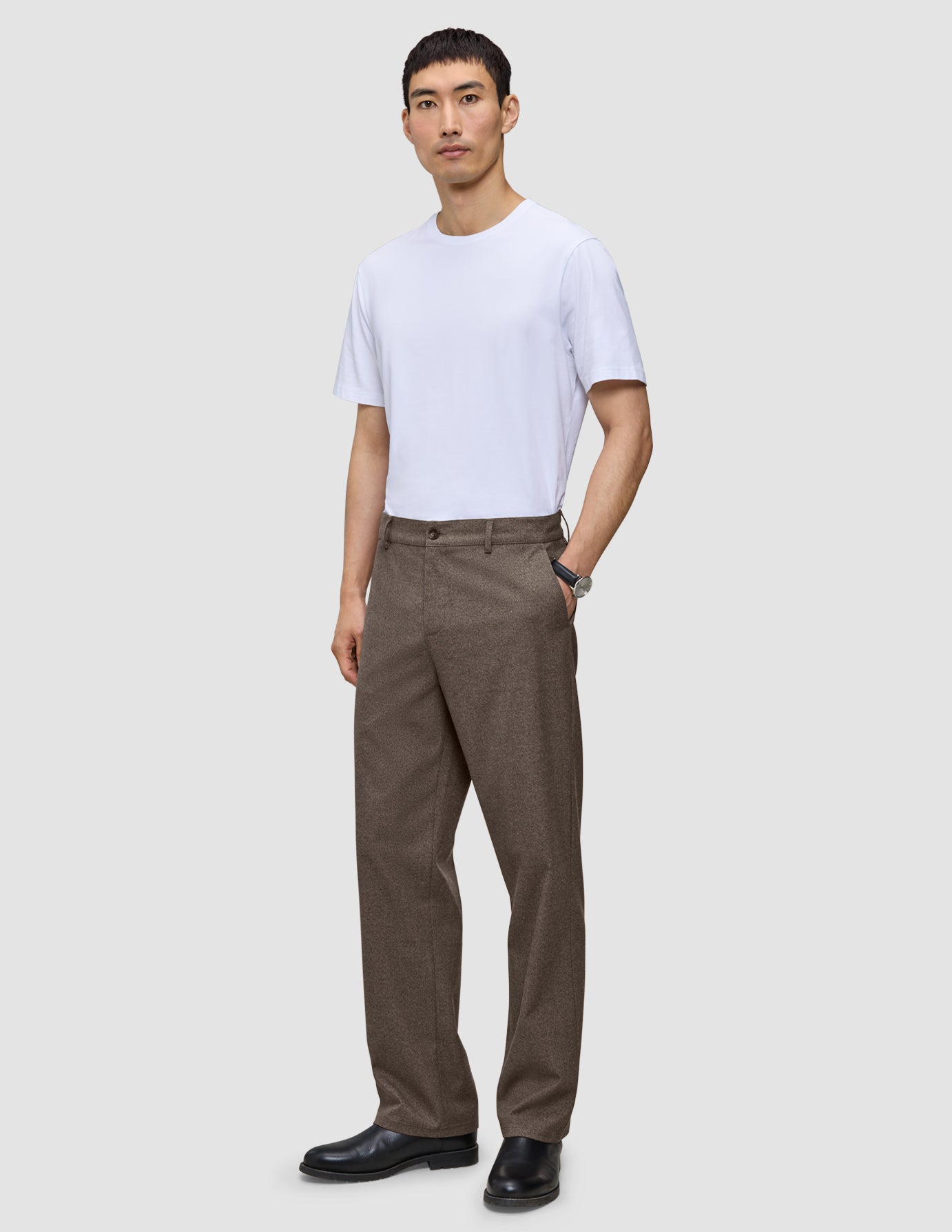 A man wearing a white t-shirt and Atelier Pants Relaxed Dark Beige in a heavyweight broken twill, finished with black leather shoes.