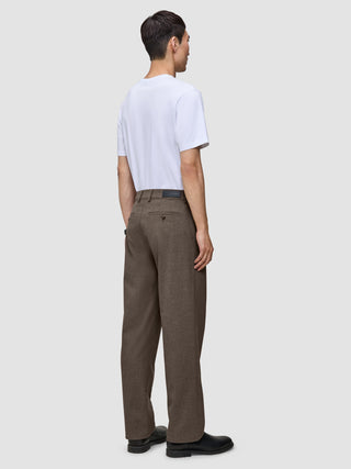 A man seen from behind wearing a white t-shirt and Atelier Pants Relaxed Dark Beige in heavyweight broken twill with black shoes.