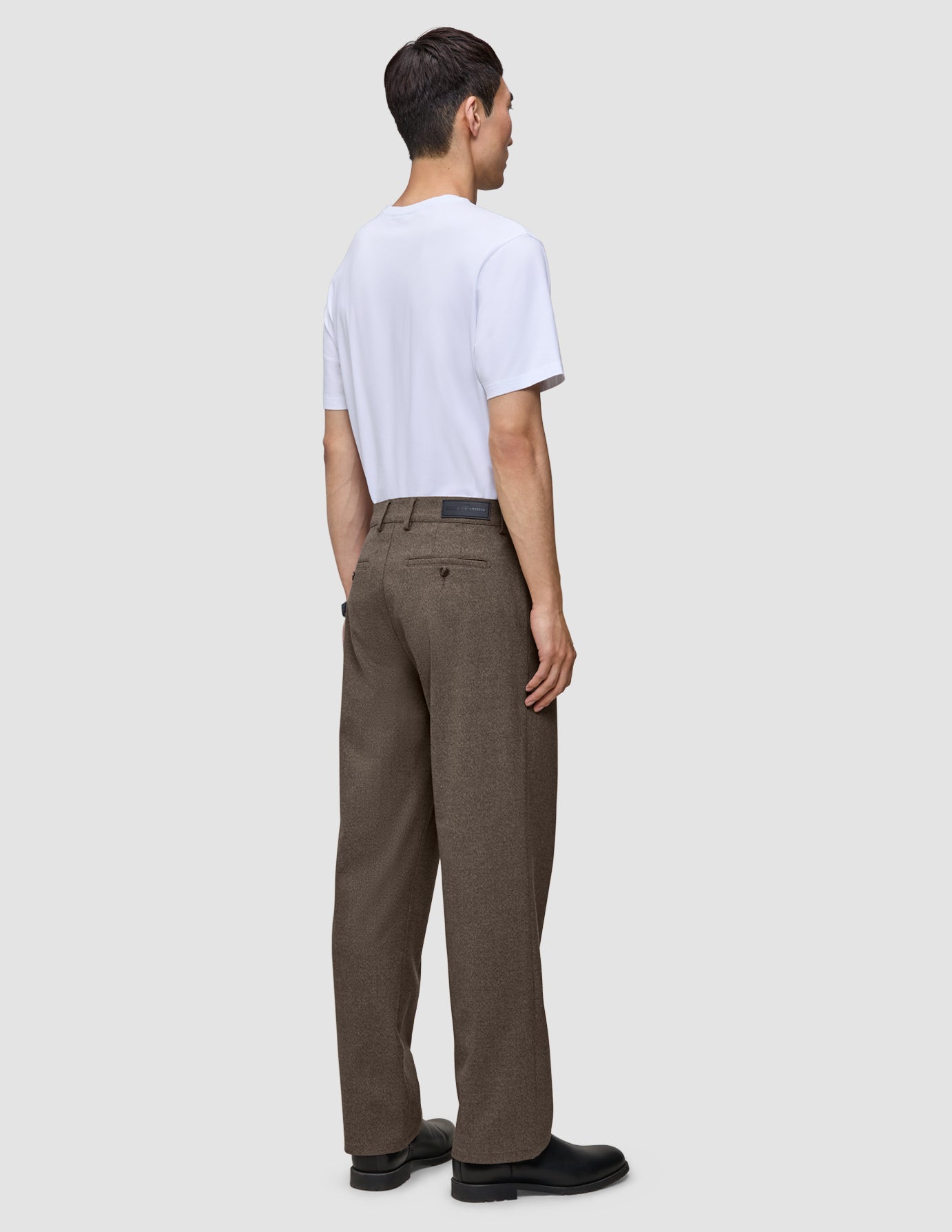 A man seen from behind wearing a white t-shirt and Atelier Pants Relaxed Dark Beige in heavyweight broken twill with black shoes.