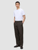 A man wearing a white t-shirt and Atelier Pants Relaxed Dark Brown in heavy-weight broken twill, standing with his hands in his pockets.